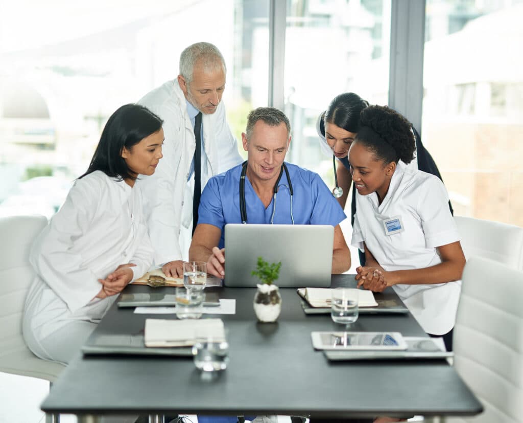 Healthcare team in uniforms gathered around a laptop at a meeting table